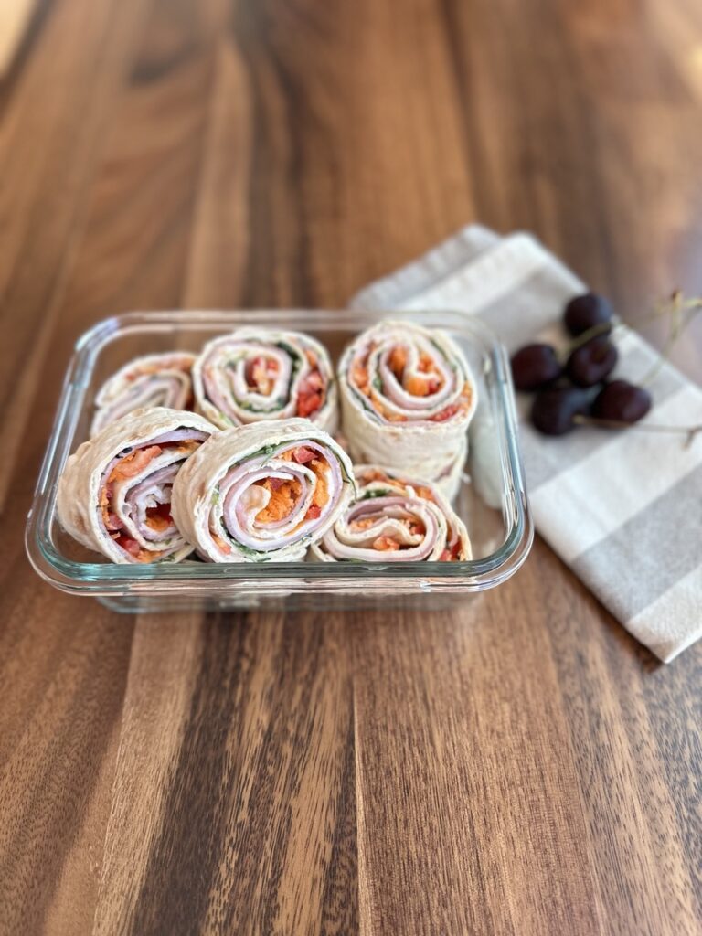 ham and cheese pinwheels packed in a lunch container with cherries on the side
