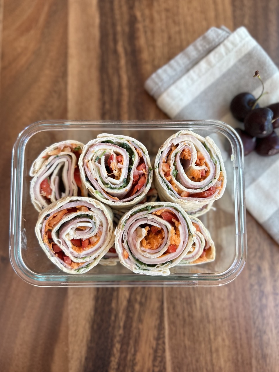 overhead photo of ham and cheese pinwheels sliced and store in a lunch container with cherries on the side